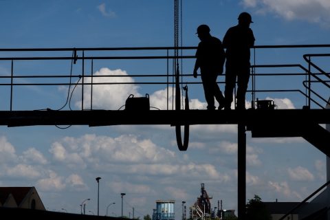 silhouette of two workers in hard hat standing on scaffolding in industrial area