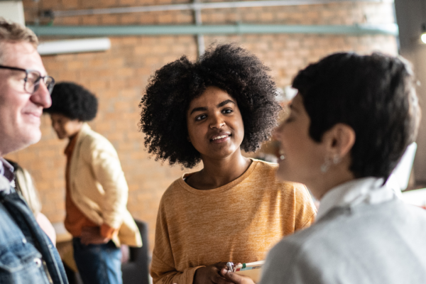 A mana and two woemn are talking in a room. Other people are in the background