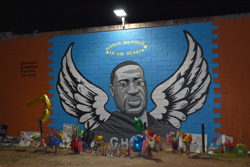 Mural in Texas of george floyd with wings and a halo over his heads. An overhead light shines down on the halo -reflecting the change his death will bring following Derek Chauvin's guilty verdict.