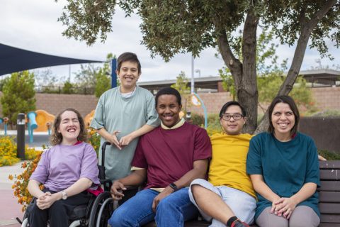 A diverse group of smilling young people with developmental disabilities hanging out together in a park, and pose for a photo
