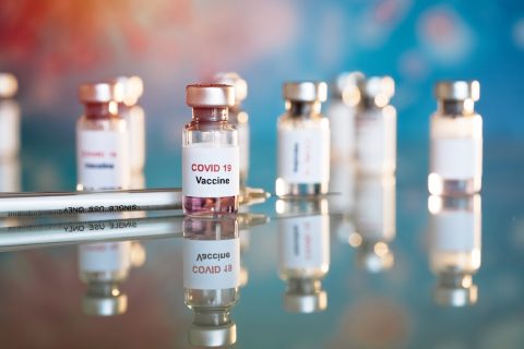 Vials of covid vaccine on reflective table with a syringe