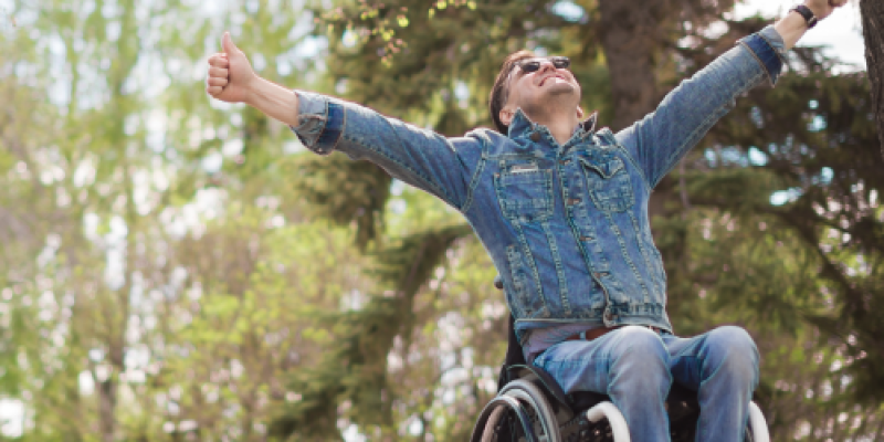 A man in a wheelchair with his hands in the air is looking up at eh size