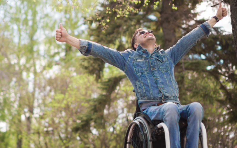 A man in a wheelchair with his hands in the air is looking up at eh size