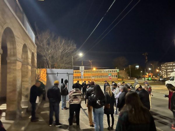 A crowd gathers to listen to a speaker with the replica cell in the background.