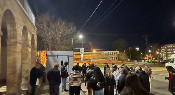 A crowd gathers to listen to a speaker with the replica cell in the background.