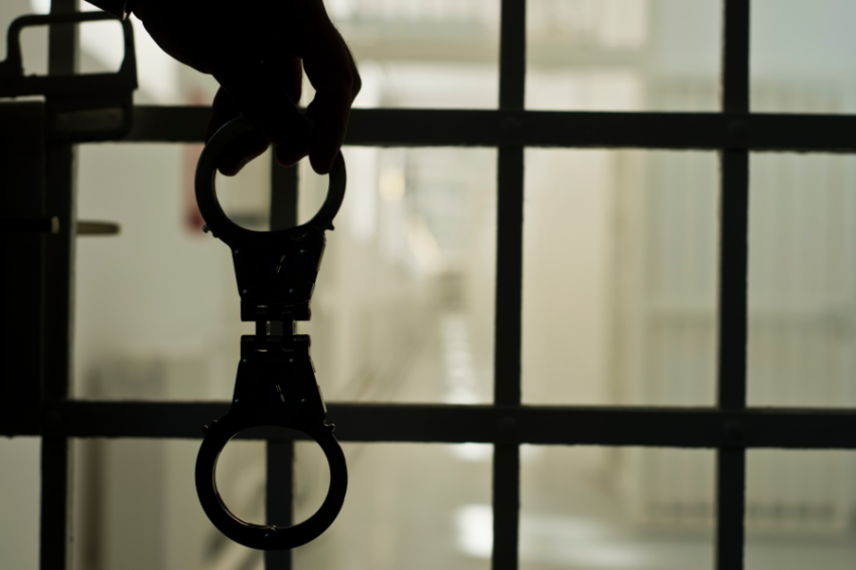 a person's hand behind the bars of a prison or jail, holding handcuffs