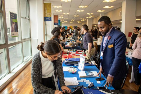 Two people in focus at an exhibitor booth in a conference style space and people behind them