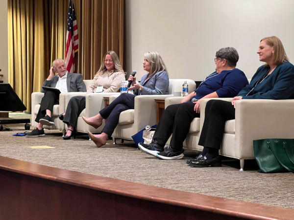 panel group at conference on a stage. One person holds a microphone while speaking