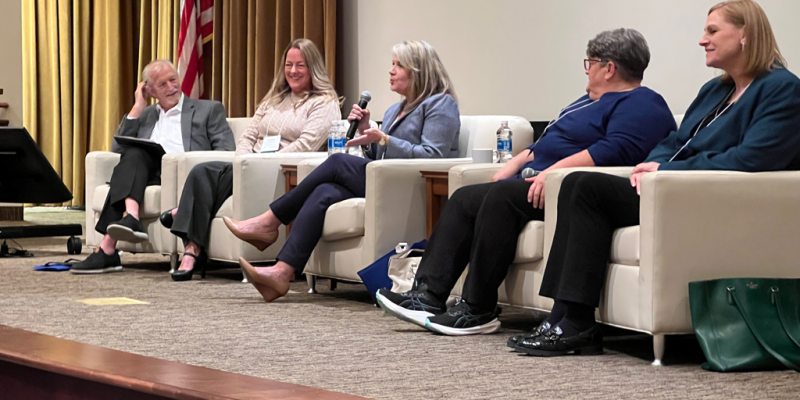 panel group at conference on a stage. One person holds a microphone while speaking