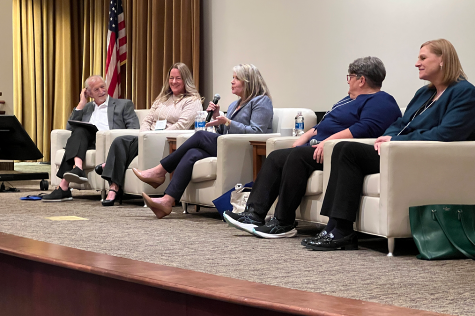 panel group at conference on a stage. One person holds a microphone while speaking