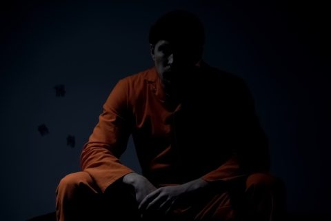 incarcerated male of color sitting in darkness of solitary confinement.