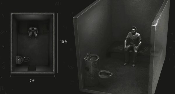 A very dark black and white overhead view of a man sitting alone in a solitary confinement cell.