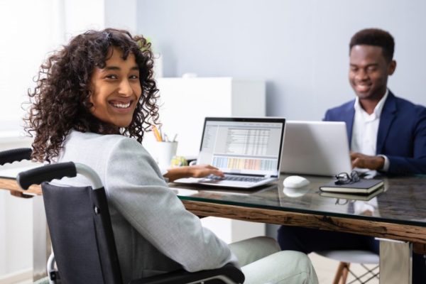 Two individuals, one is a wheelchair user, at desk.