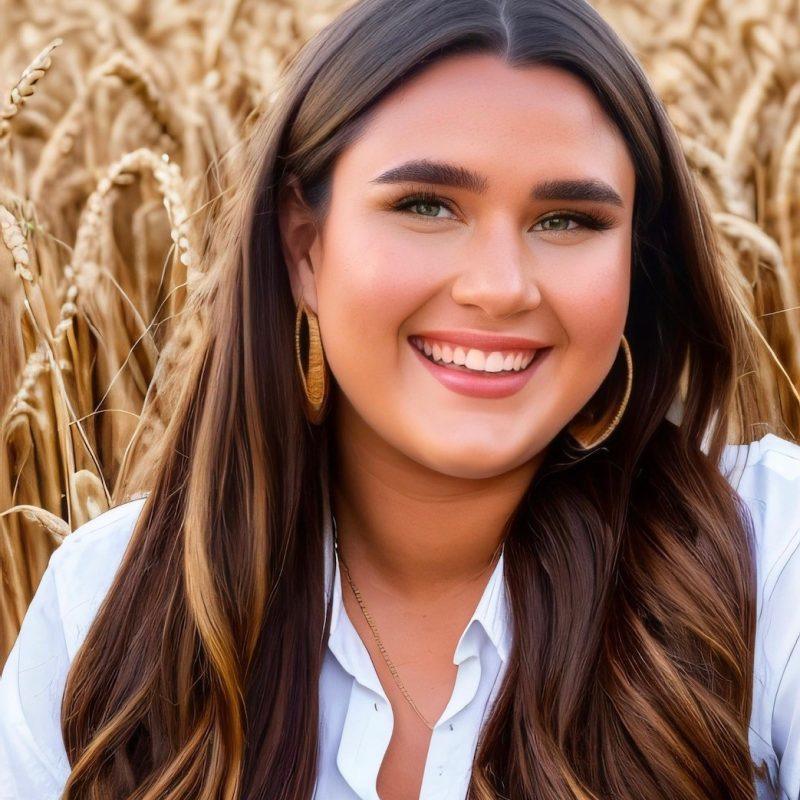 A smiling woman with a white shirt and long hair in a field of wheat