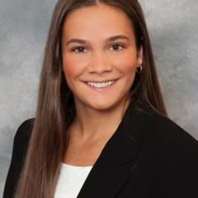 Headshot of a young woman with long brown hair in a white blouse and black jacket