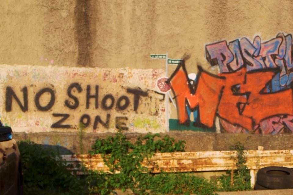 A concrete wall on the side of the road rises up from the ground with graffiti on the right side and the words 